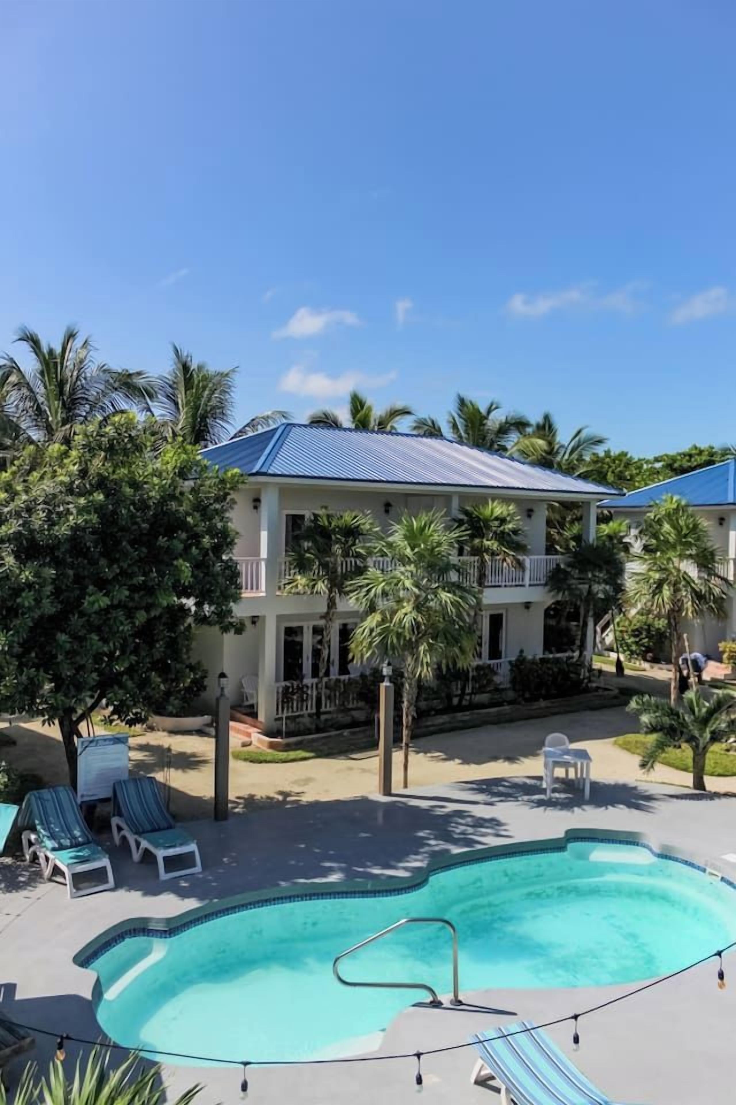 A two-story building with a swimming pool, lounge chairs, and palm trees.