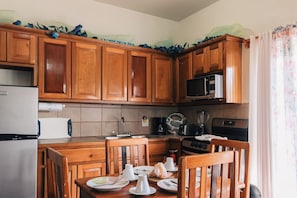 A kitchen with wooden cabinets, a microwave, a stove, and a dining table set with plates and cups.