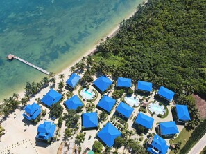 An aerial view of a resort with multiple blue-roofed buildings, a beach, and a pier.