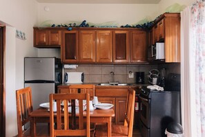 A compact kitchen with wooden cabinets, a refrigerator, a microwave, a stove, and a dining table with chairs.