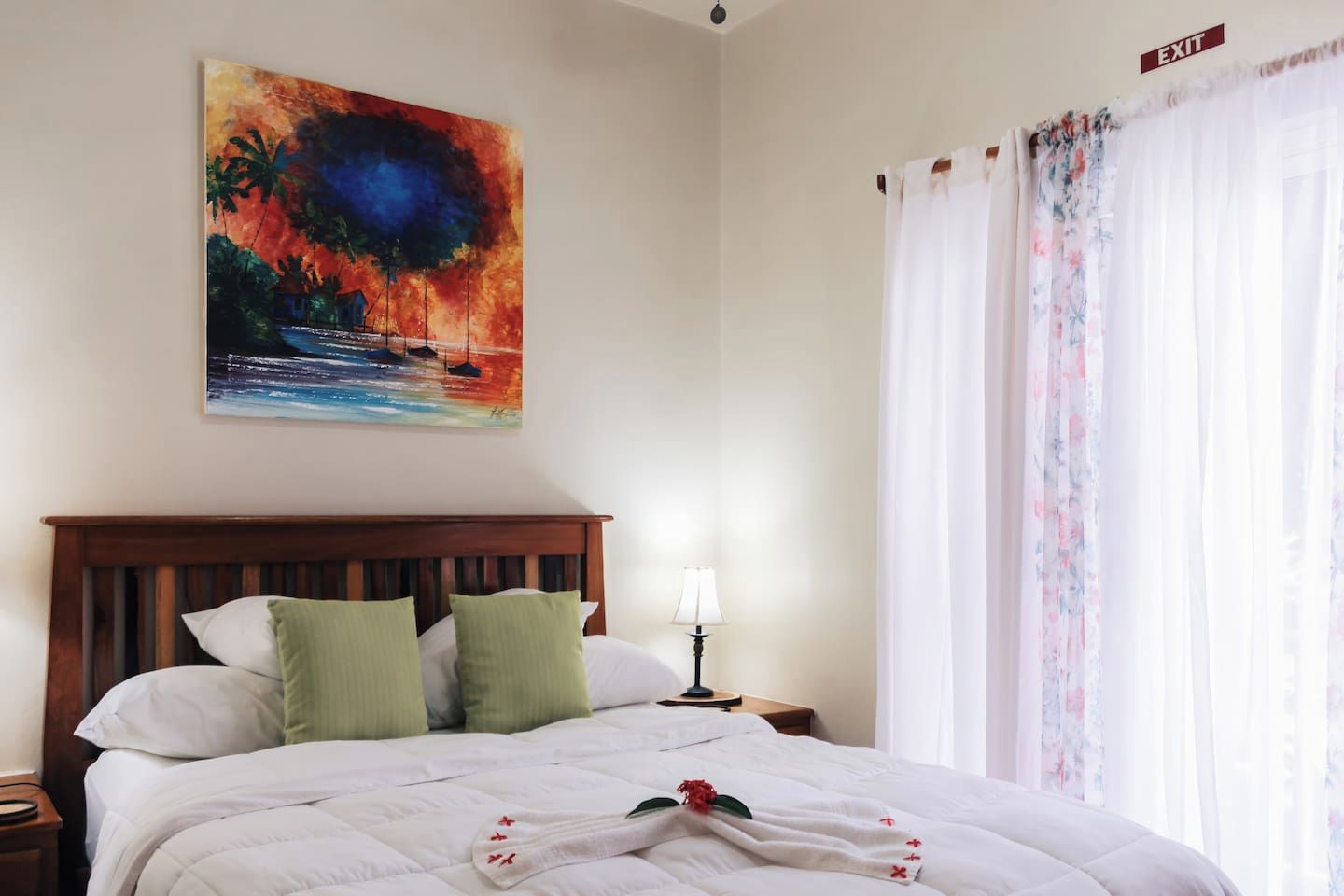 A hotel room with a bed, a nightstand, a lamp, a painting, and a window with curtains.