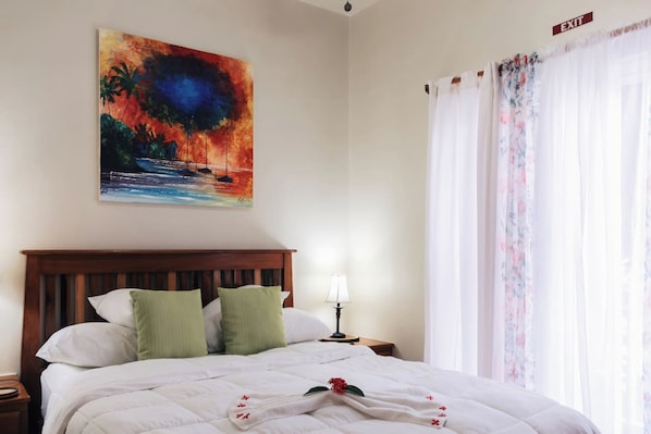 A hotel room with a bed, a nightstand, a lamp, a painting, and a window with curtains.