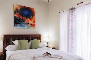 A hotel room with a bed, a nightstand, a lamp, a painting, and a window with curtains.