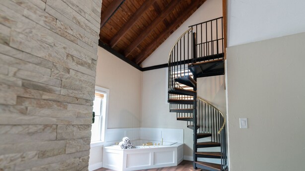 Una habitación con pared de piedra, un banco blanco empotrado, una bañera y una escalera de caracol.
