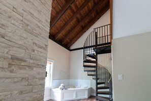 A room with a stone wall, a white built-in bench, a bathtub, and a spiral staircase. - Chimney Hill - 03) Second Floor Suite 3 (Lambertville)