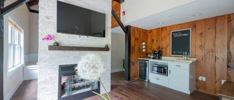 A modern kitchen with a stone fireplace, wooden accents, and a welcome sign.