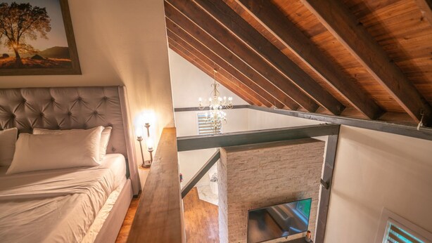 Een slaapkamer met een bed, nachtkastje, lamp en een televisie bevestigd aan een stenen muur.