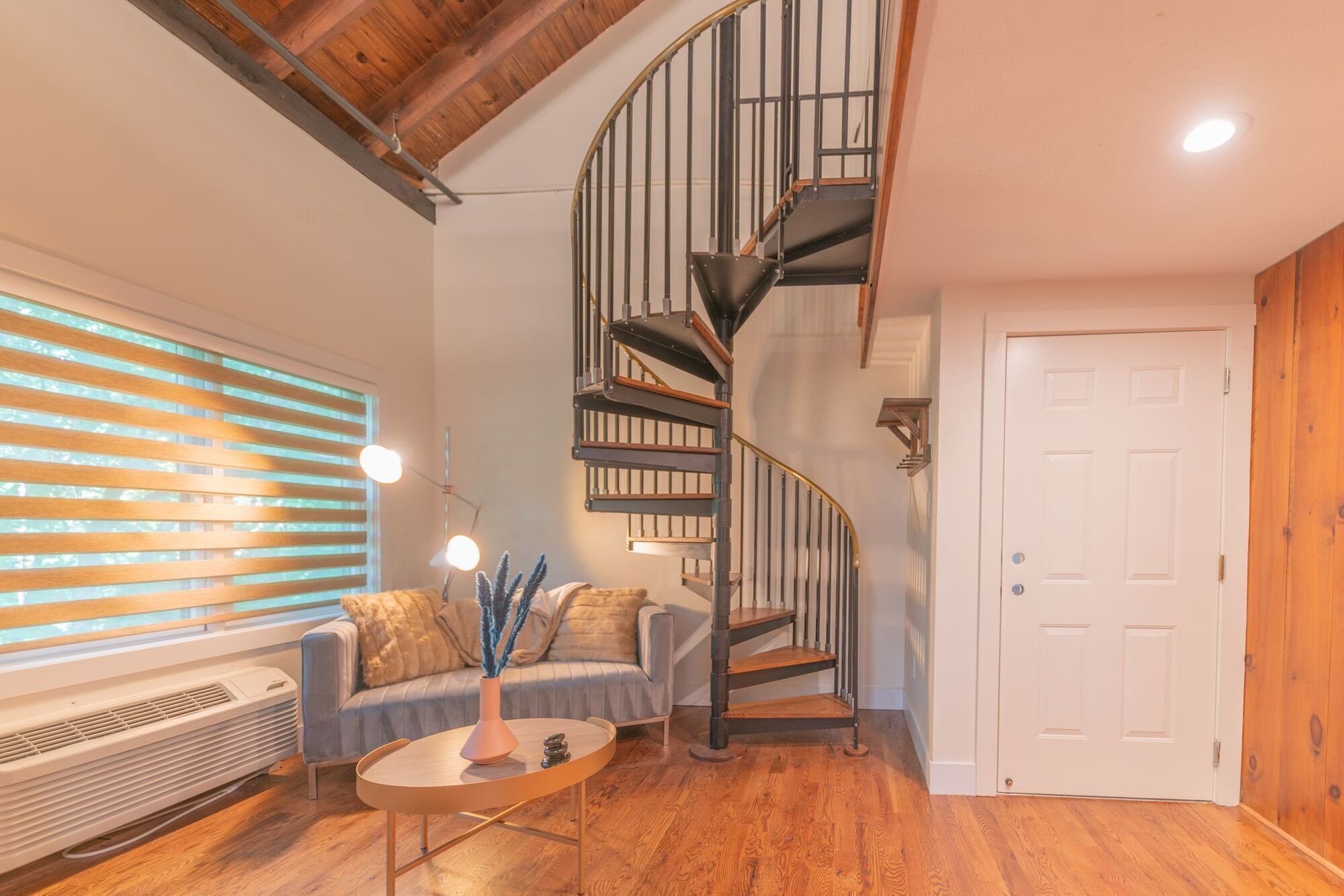 A living room with a curved staircase, a sofa, a coffee table, and a door.