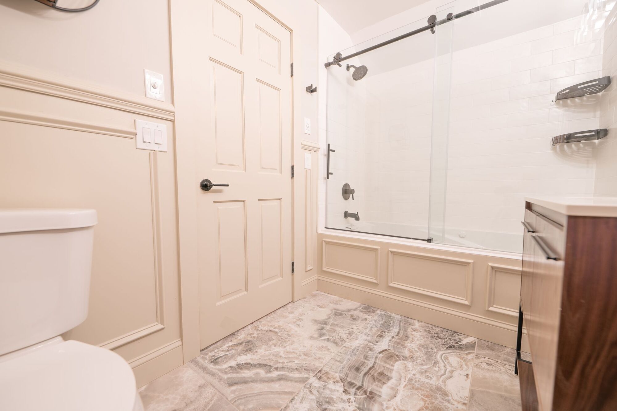 A bathroom with a toilet, a shower with a glass door, and a marble floor.