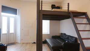 Um quarto com uma cama beliche, um sofá, uma escada, uma porta e uma janela.