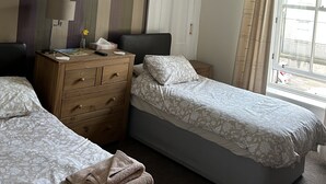 Una habitación de hotel con dos camas individuales, un aparador de madera, un escritorio con lámpara y una ventana con cortinas.