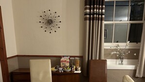 Habitación de hotel con una mesa de comedor para dos personas, un reloj en la pared y una ventana con cortinas.