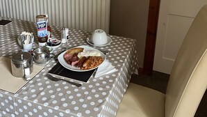 Una mesa de comedor con mantel de lunares, un plato de comida, condimentos y una tetera.