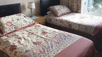 A hotel room with two beds, a nightstand with a lamp, and a window with curtains.
