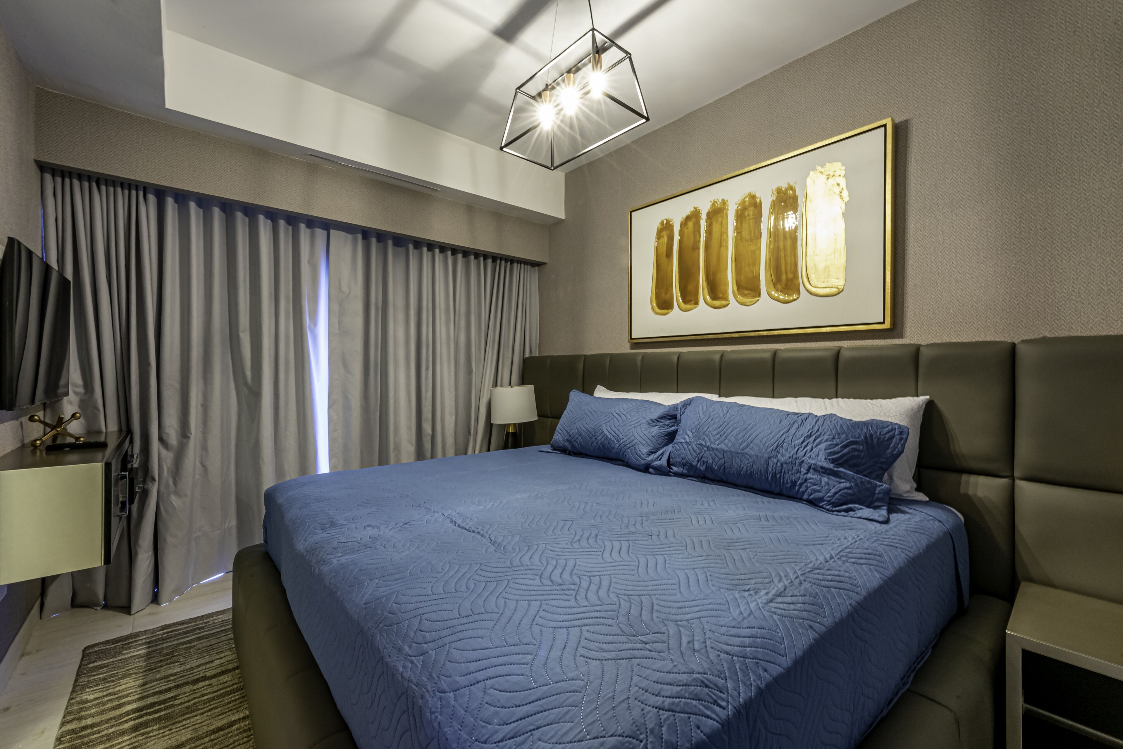 Een moderne hotelkamer met een groot bed, een flatscreen televisie, een bureau en een kunstwerk in een lijst aan de muur.