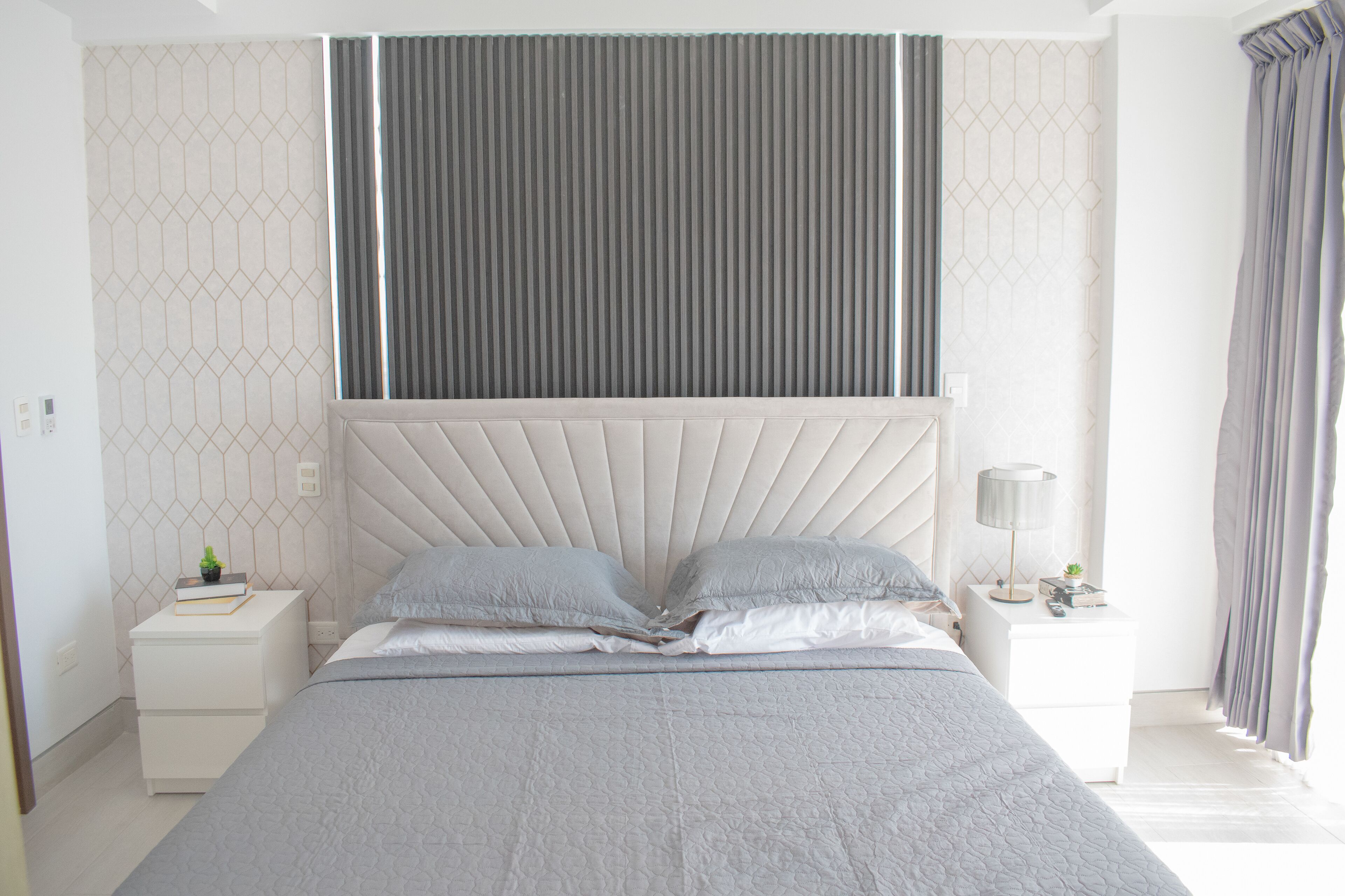 Une chambre moderne avec un grand lit, deux tables de chevet, une commode, une lampe et un rideau.