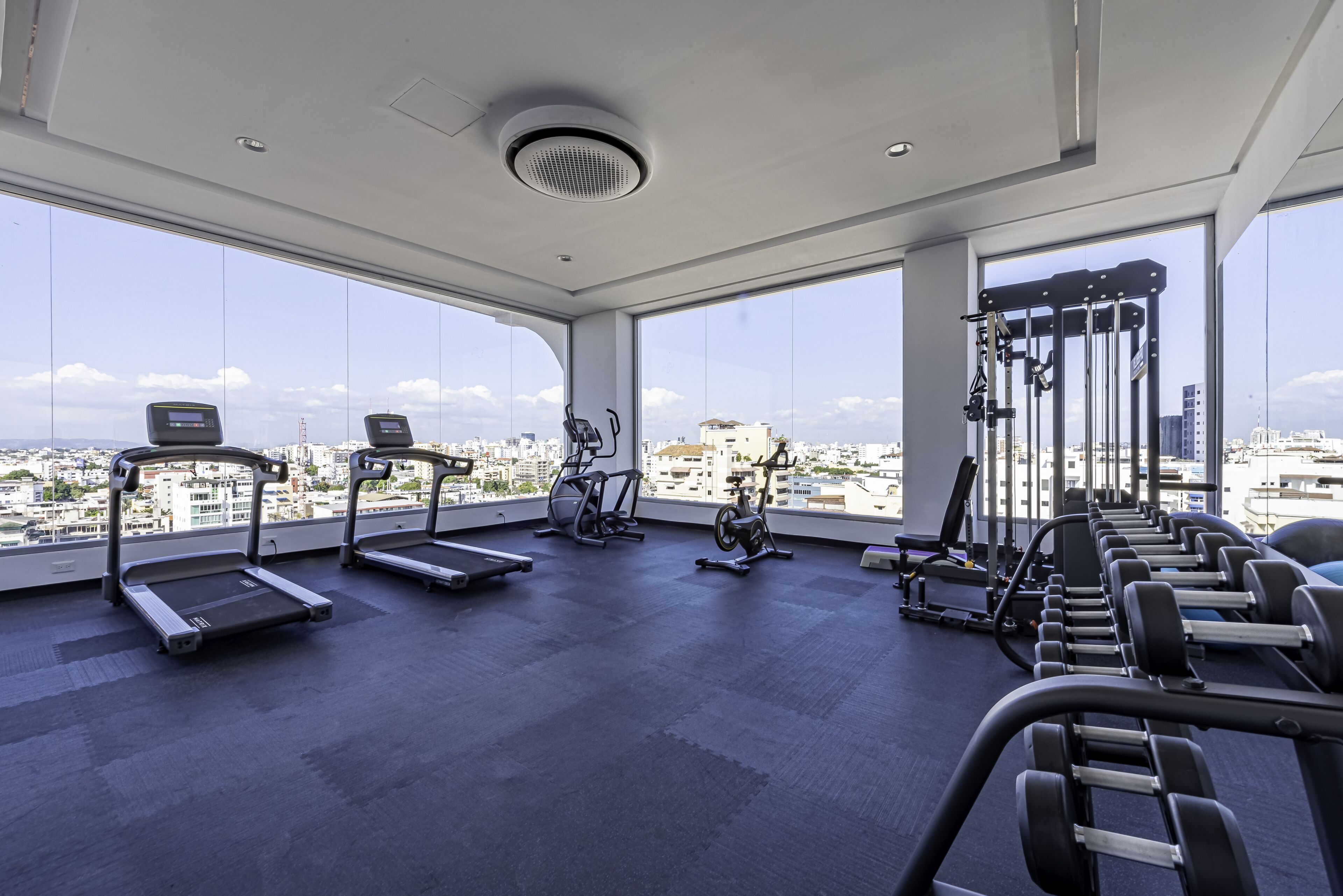 A gym with treadmills, stationary bikes, and weight machines, large windows with a city view.