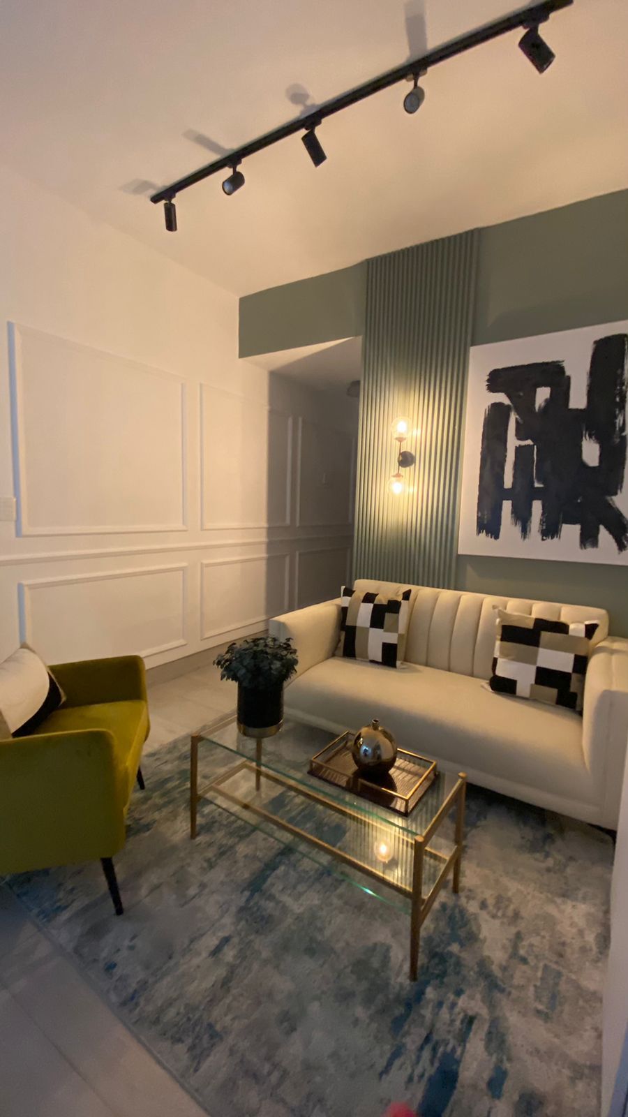 A modern living room with a sofa, a yellow armchair, a glass coffee table, and a large abstract painting.