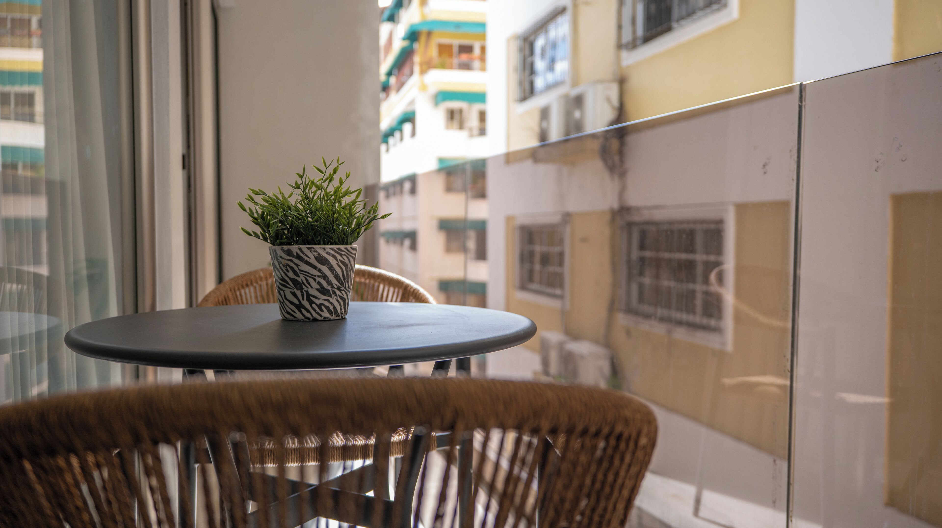 A balcony with a round table, a wicker chair, and a potted plant.