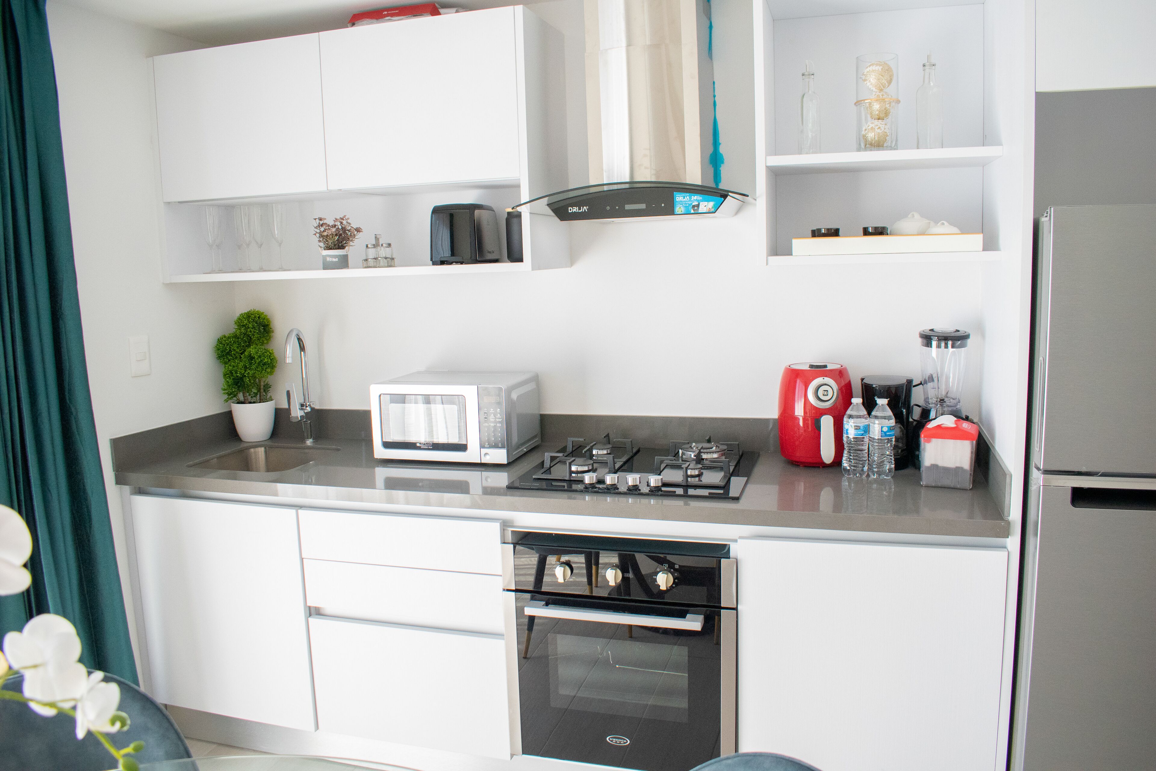 Een moderne keuken met witte kastjes, een gasfornuis, een magnetron en een koelkast.