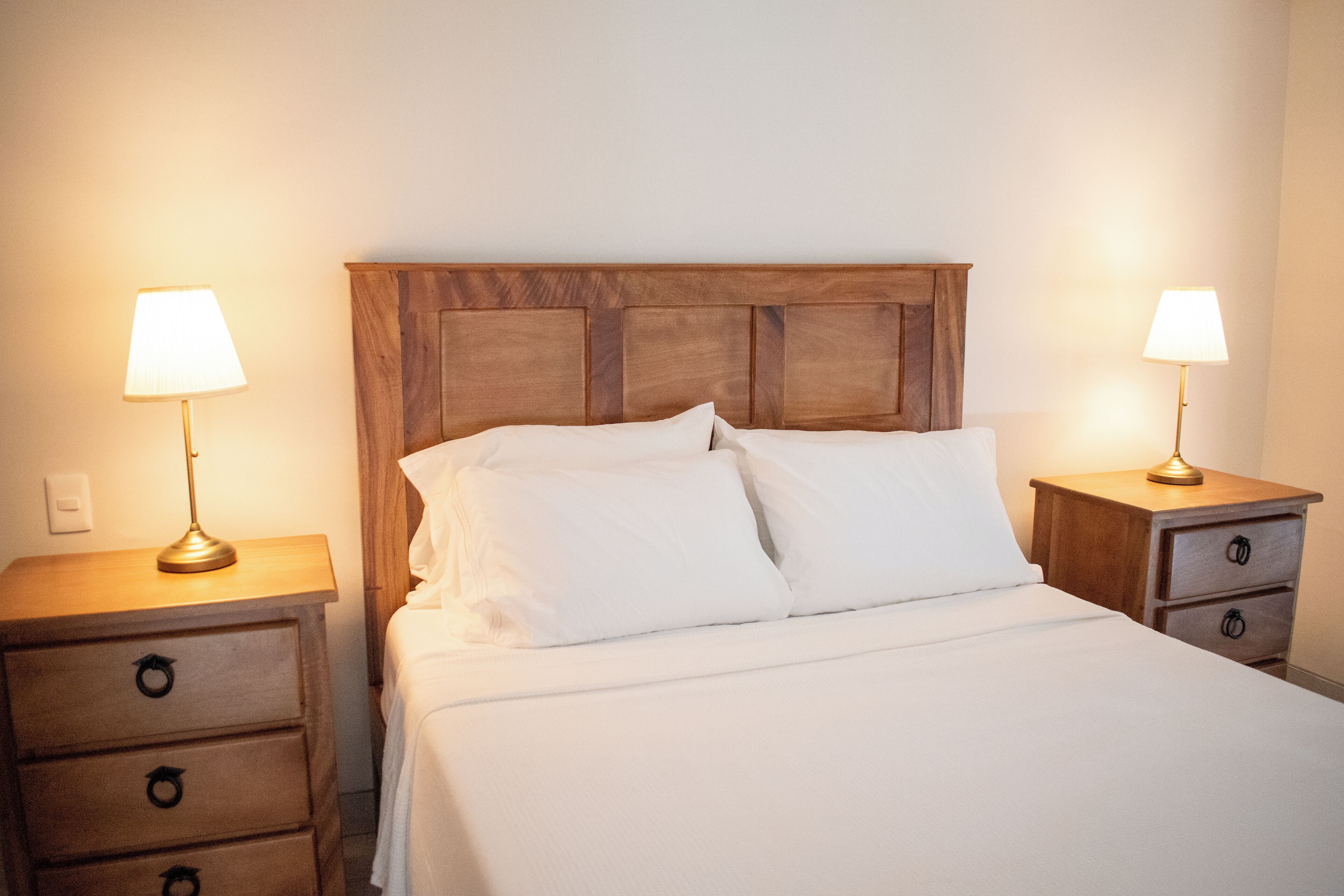 A neatly made bed with white linens, two bedside tables with lamps, and a wooden headboard.