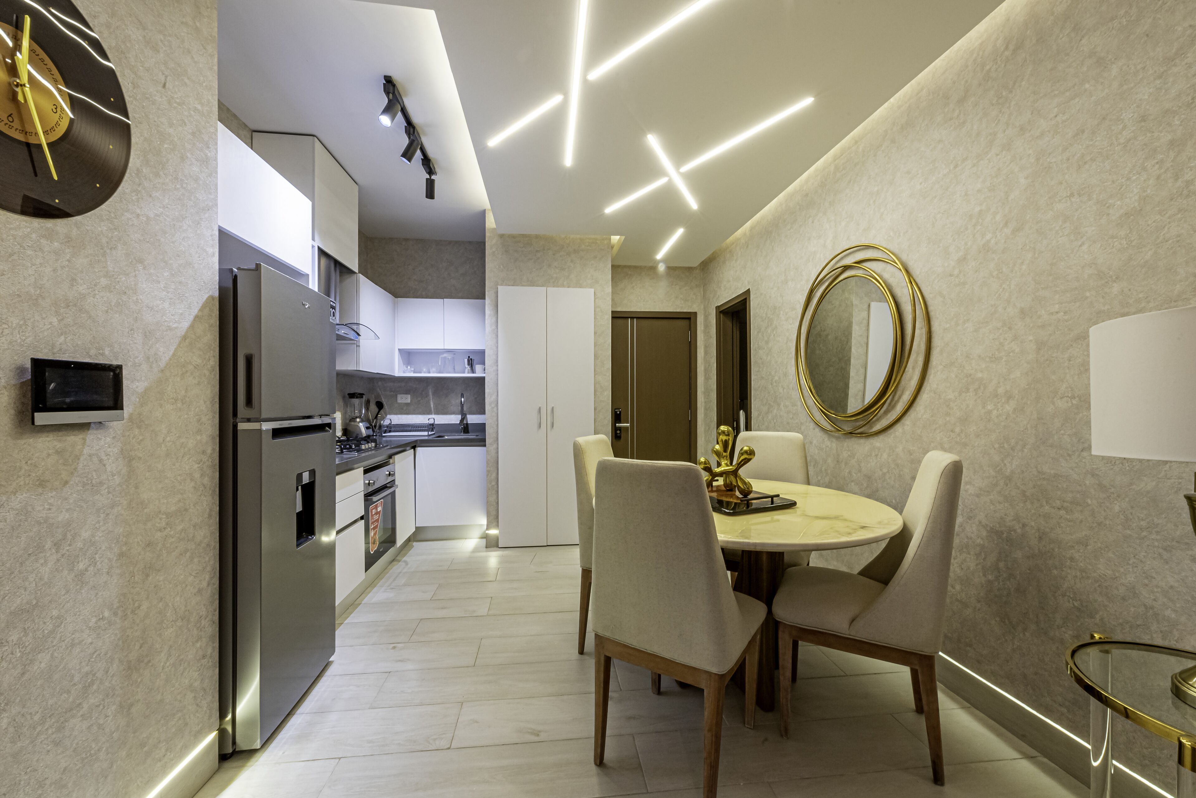 A modern kitchen with a built-in refrigerator, a dining area with a round table and chairs, and a wall-mounted mirror.
