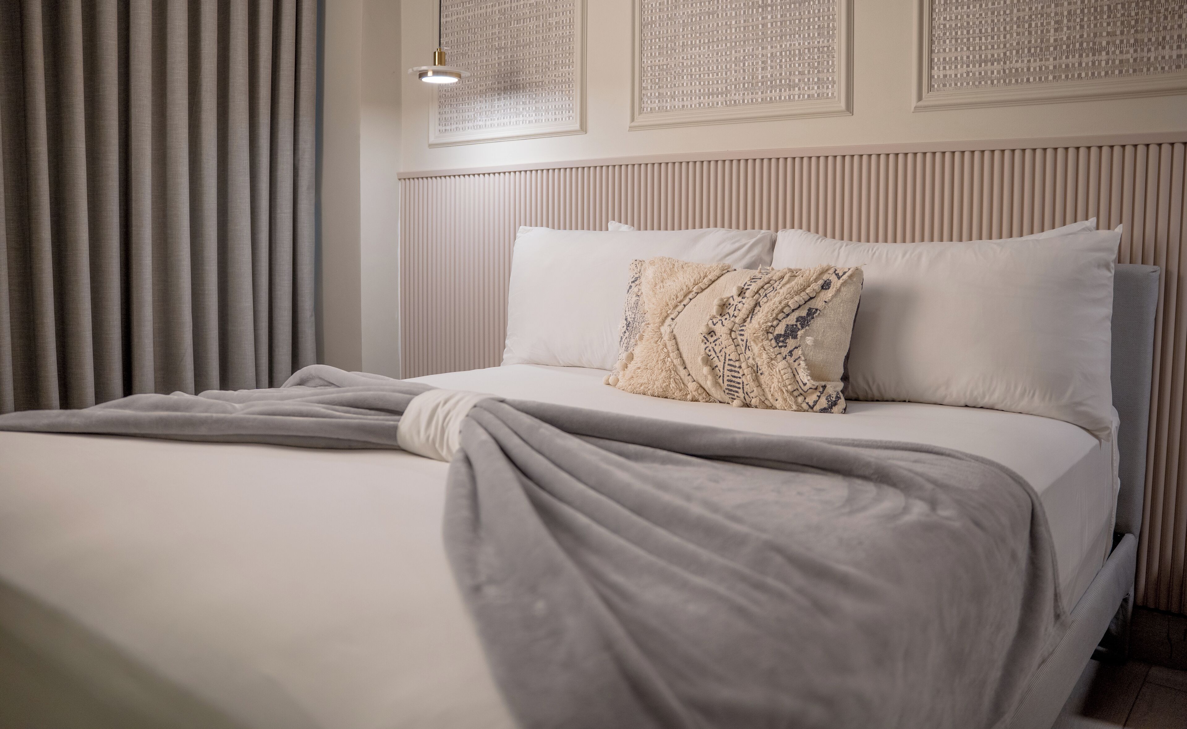 Una cama bien hecha con un edredón gris, almohadas blancas y un cojín decorativo.