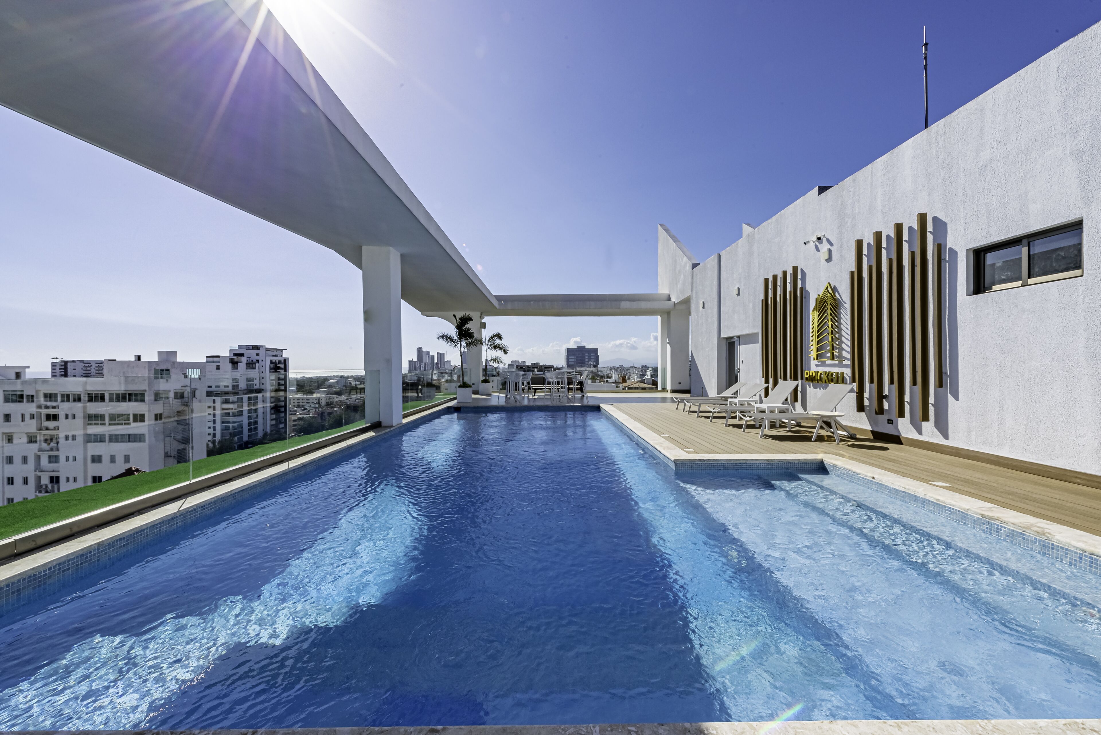 A modern pool area with a clear view of the city skyline, a covered walkway, and a section with lounge chairs.