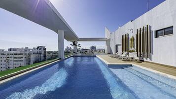 A modern pool area with a clear view of the city skyline, a covered walkway, and a section with lounge chairs.