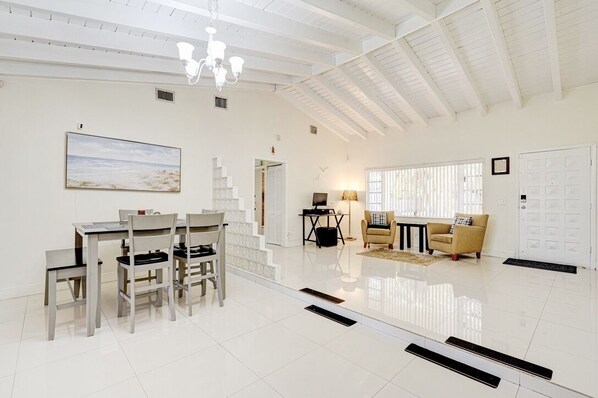 A spacious living area with a dining table and chairs, a sofa, a lamp, and a painting on the wall.