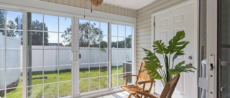 A sunroom with a sliding glass door, a ceiling fan, wooden chairs, and a potted plant.