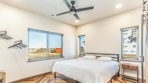 Une chambre avec un lit, un ventilateur de plafond et de grandes fenêtres donnant sur un chantier de construction.