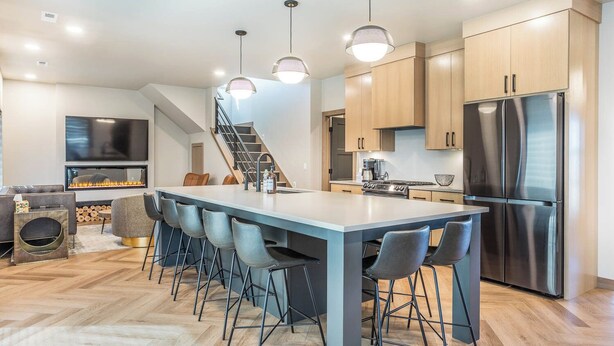 Une cuisine moderne dotée d’un îlot central, d’appareils électroménagers en acier inoxydable et d’un escalier menant à un autre niveau.