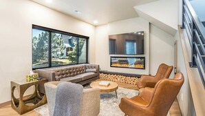 Un salon moderne doté d’une grande fenêtre, d’une cheminée, d’un canapé et de deux fauteuils en cuir.