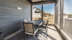 Un espace de restauration extérieur moderne, avec une table et des chaises en bois, un ventilateur de plafond et une vue sur une maison en construction.