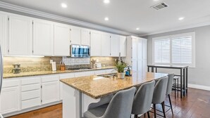 Una cocina moderna con gabinetes blancos, encimeras de granito y una isla central con taburetes de bar.