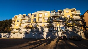 Un immeuble résidentiel à plusieurs étages, doté de balcons, d’une allée pavée et de voitures garées.