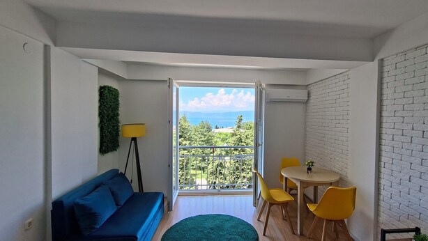 Une chambre avec un balcon, un canapé, une table avec des chaises et un téléviseur fixé au mur.