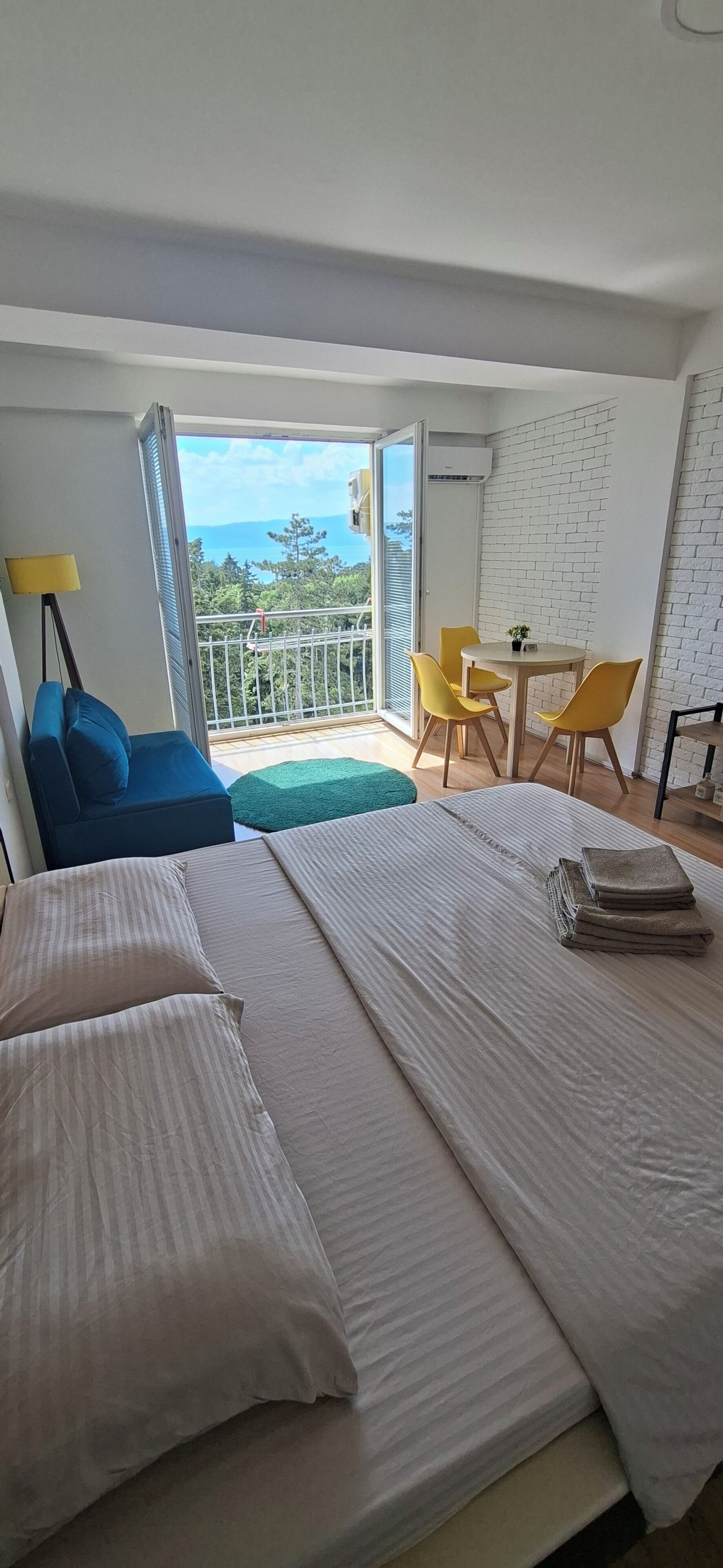 Une chambre d’hôtel avec un lit, un canapé, un balcon avec une table et des chaises, et une vue sur la mer.