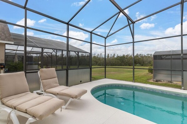 Un área de piscina con dos sillones de descanso y una estructura de vidrio.