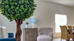Ein Wohnzimmer mit einem Kübelbaum, einem blauen Sofa, einem weißen Sessel und einem Holzschrank.