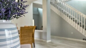 Ein modernes Interieur mit einer weißen Treppe, einem Holztisch und einer gestreiften Vase mit violetten Blumen.