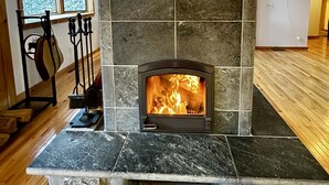 Ein Kamin aus Stein mit Feuer, in einem Zimmer mit Holzbalken und einem Fenster.
