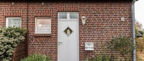 Una casa de ladrillo con una puerta blanca, una ventana pequeña con cortinas de encaje y el número 10 en la pared.
