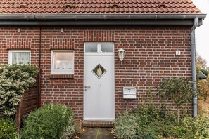 A brick house with a white door, a small window with lace curtains, and a number '10' on the wall.