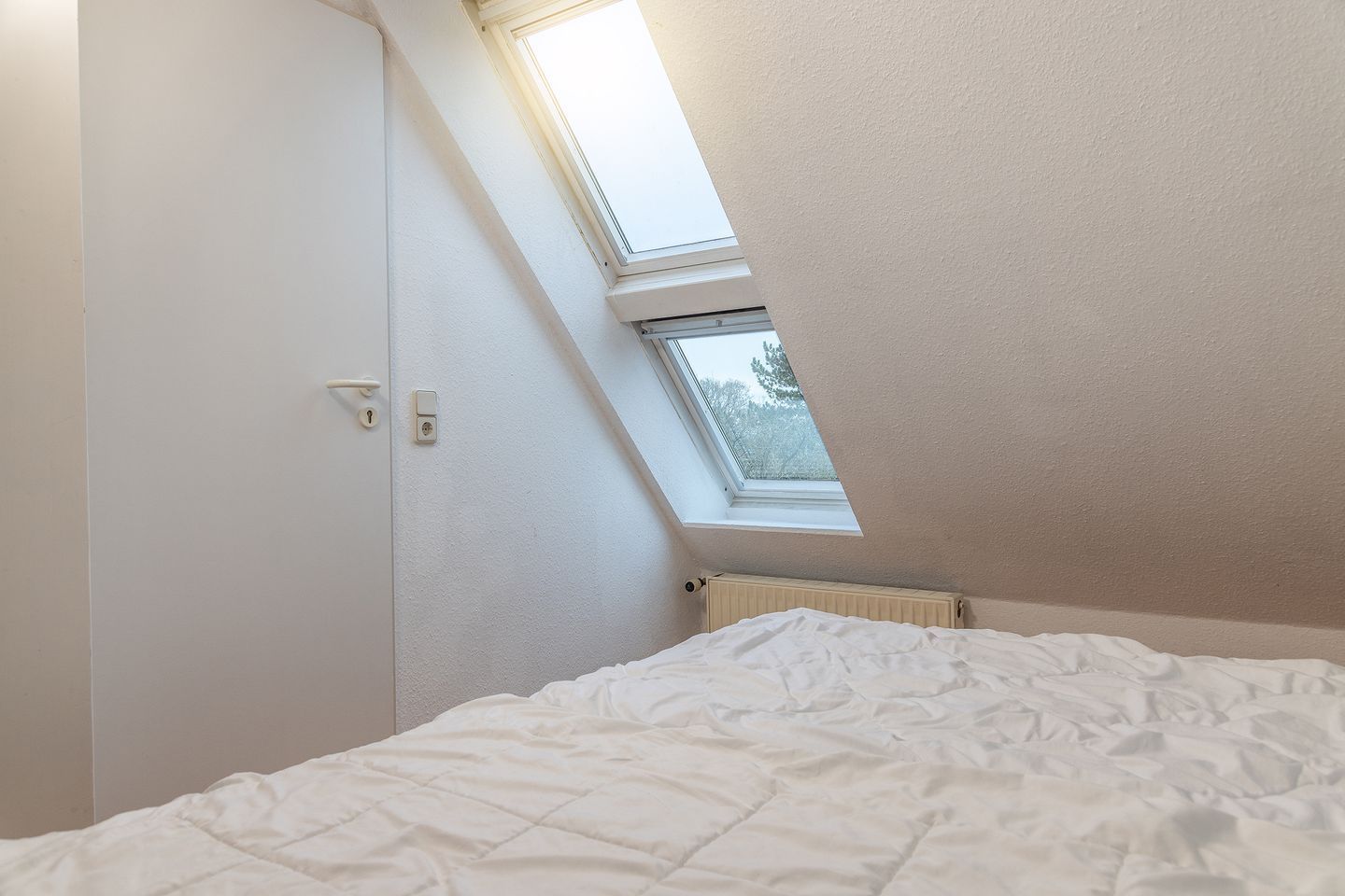 Un dormitorio con techo inclinado, tragaluz, cama y radiador.