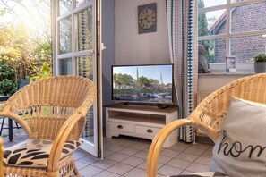 A cozy outdoor seating area with wicker chairs and a television on a wooden stand. - 50010 Ferienhaus Eulennest - Das Ferienhaus "eulennest" mit 70 qm Wohnfläche Bietet Ausreichend (Wittmund)