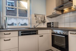 A kitchen with a dishwasher, microwave, and oven. - 50010 Ferienhaus Eulennest - Das Ferienhaus "eulennest" mit 70 qm Wohnfläche Bietet Ausreichend (Wittmund)