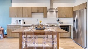 A modern kitchen with wooden cabinets, a stainless steel refrigerator, and a dining area with clear chairs. - Stylish downtown condo w/pool & parking (Nashville)