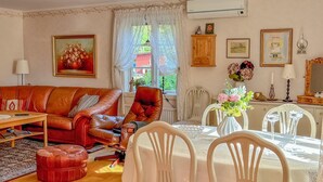 A living room with a brown leather sofa, a red armchair, a wooden cabinet, a dining table with white chairs, and a vase with flowers.